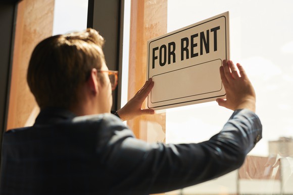 man with glasses posting for rent sign on a window