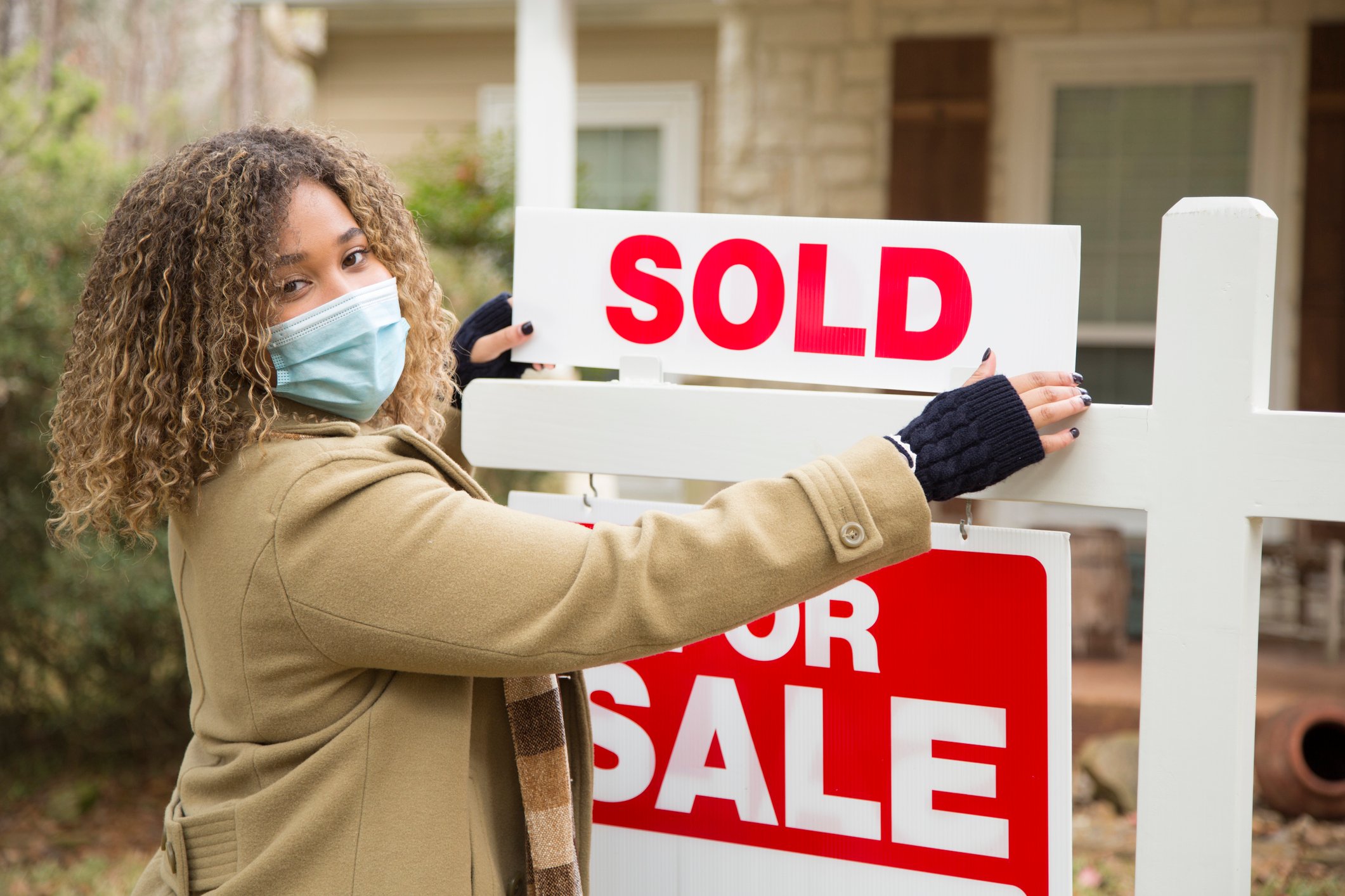 woman with face mask on putting up sold sign in a yard