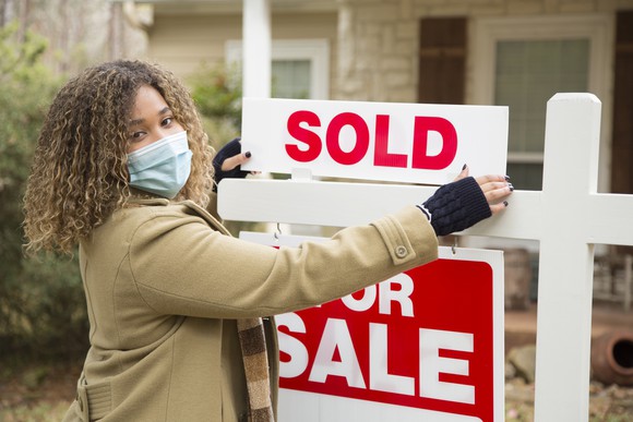 woman with face mask on putting up sold sign in a yard