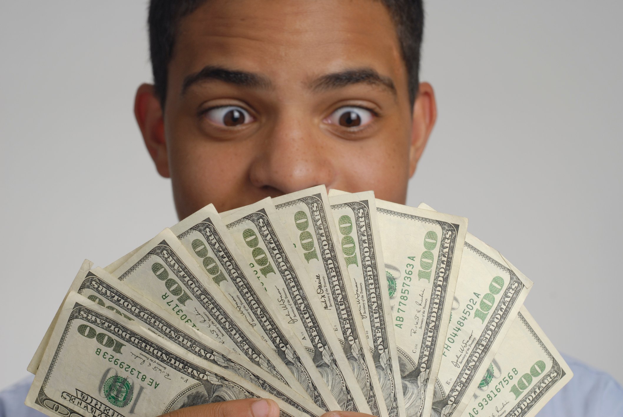 A man looks at $100 bills fanned out in front of his face.