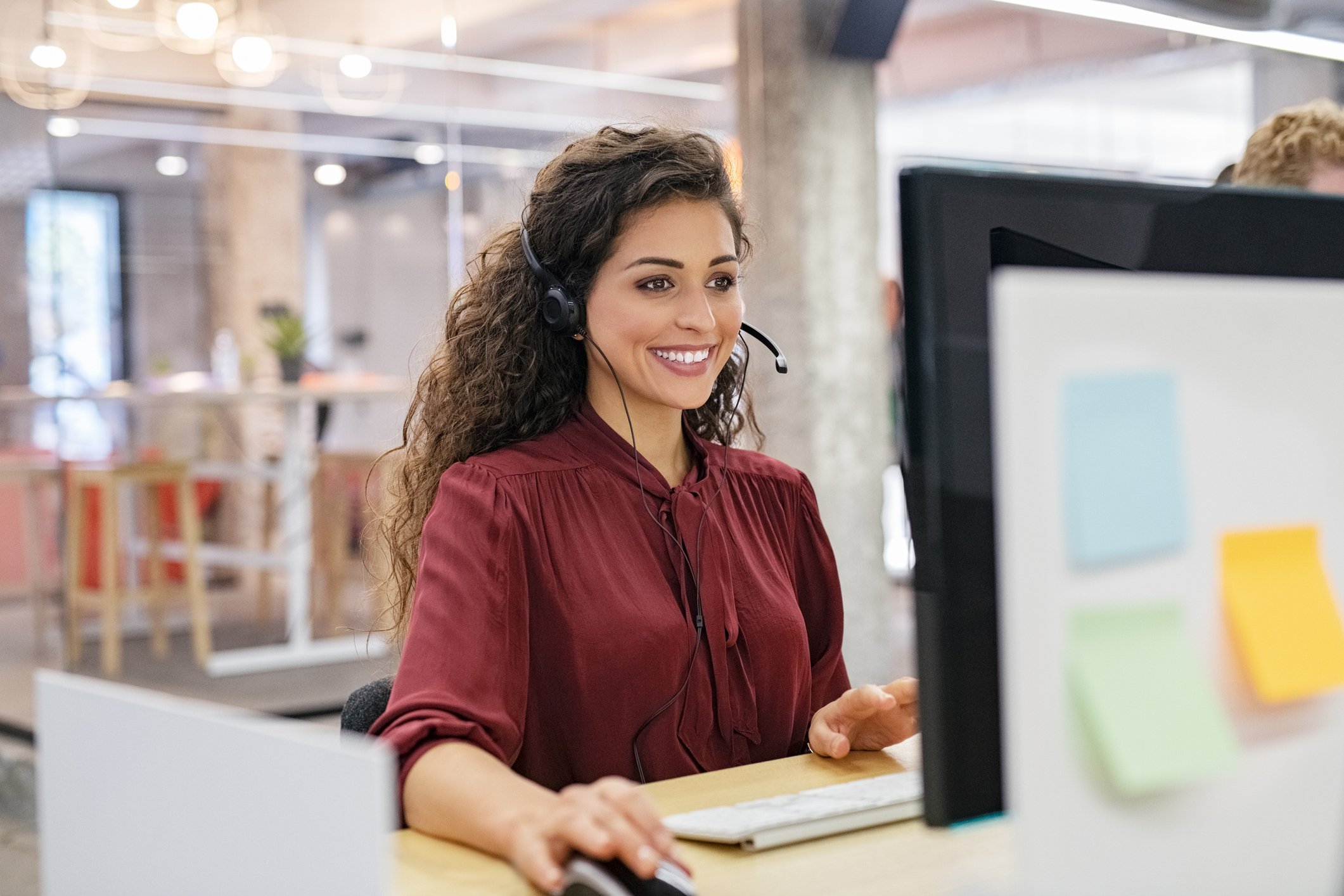 Smiling sales person on a phone headset looking at a computer.