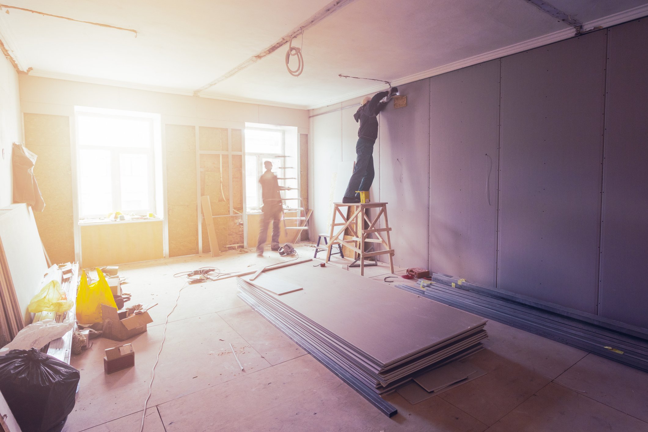 Workers install interior wallboards at a construction site.