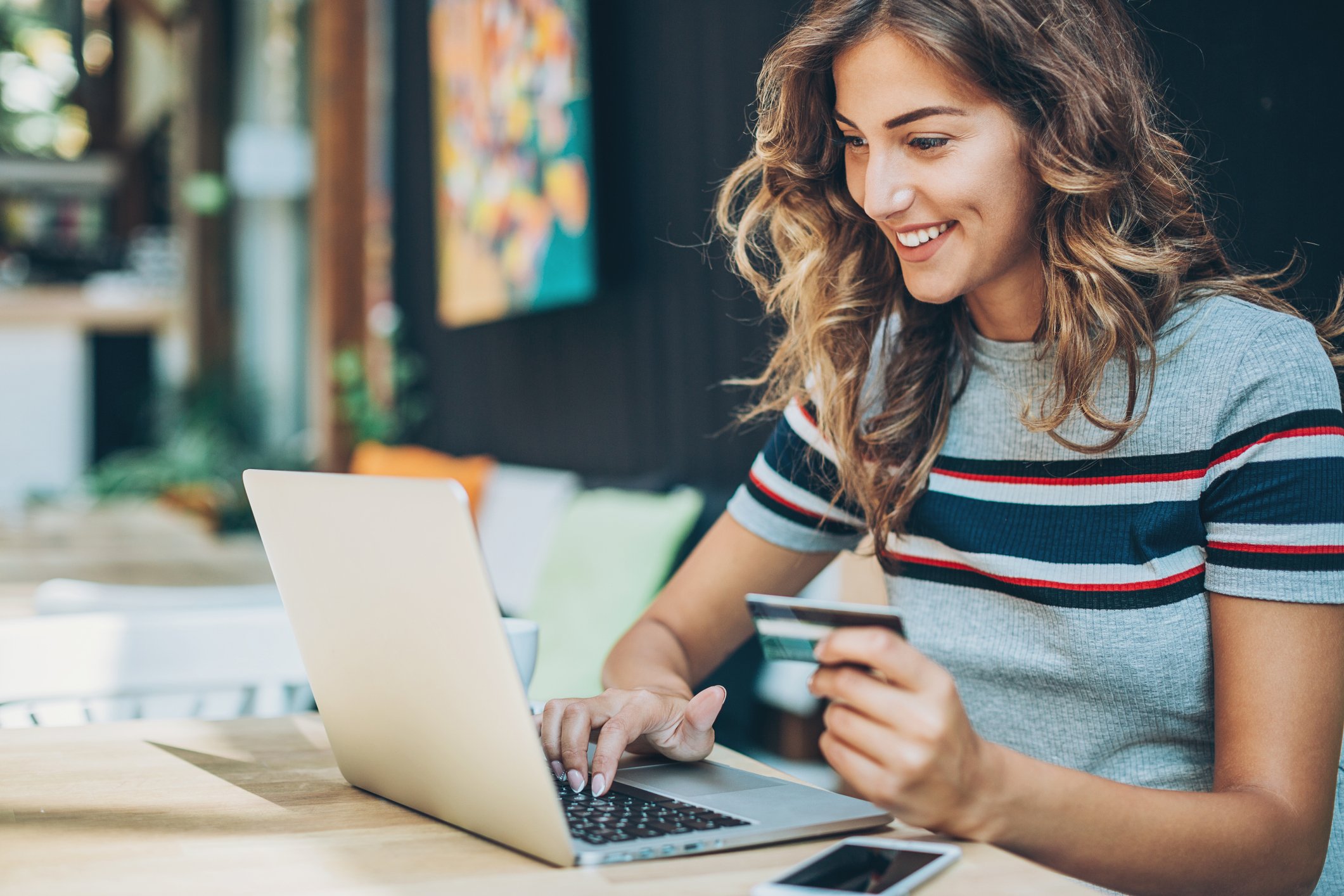 An online shopper holds a credit card while using a laptop at home.