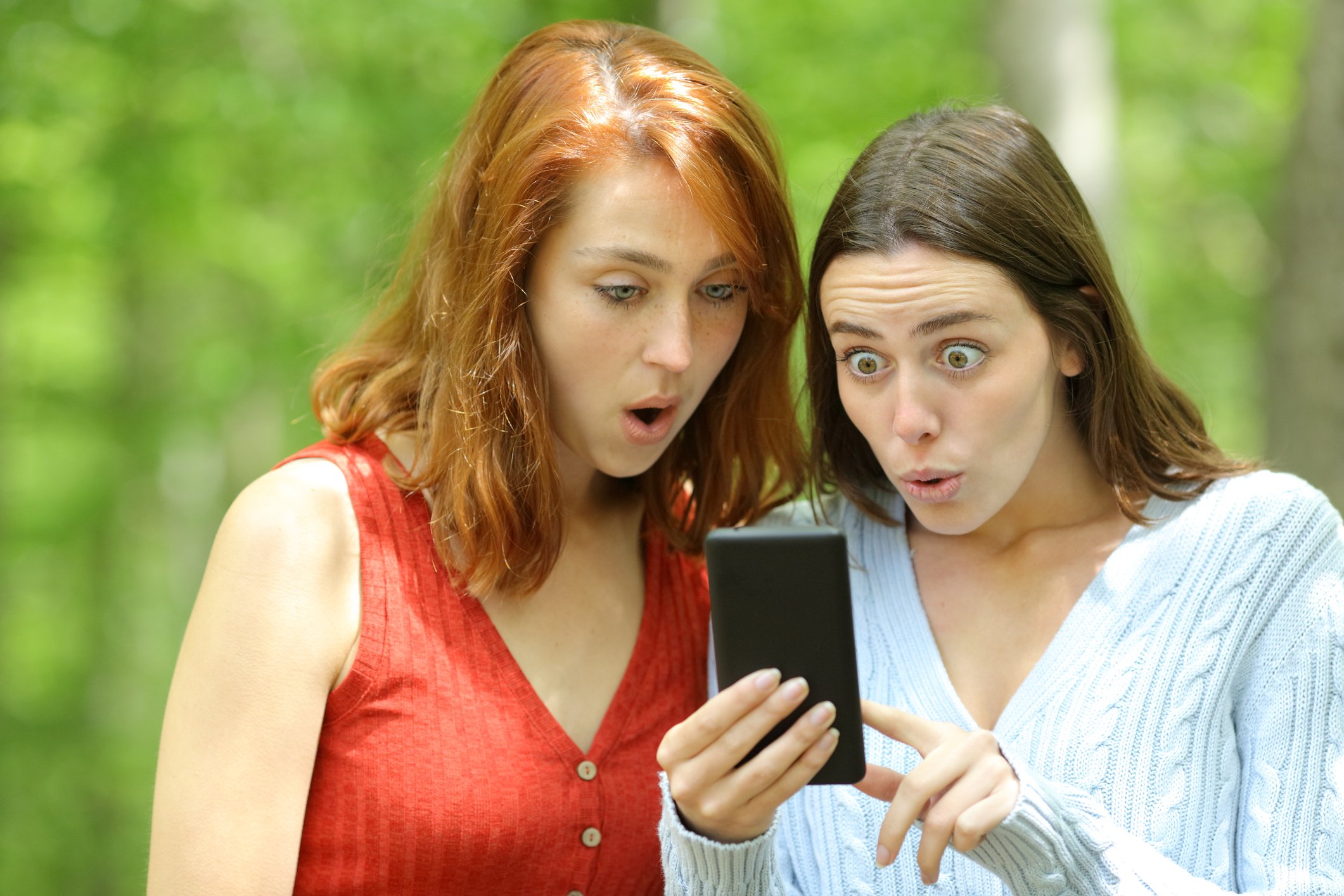 Two women looking at a phone with surprised looks.