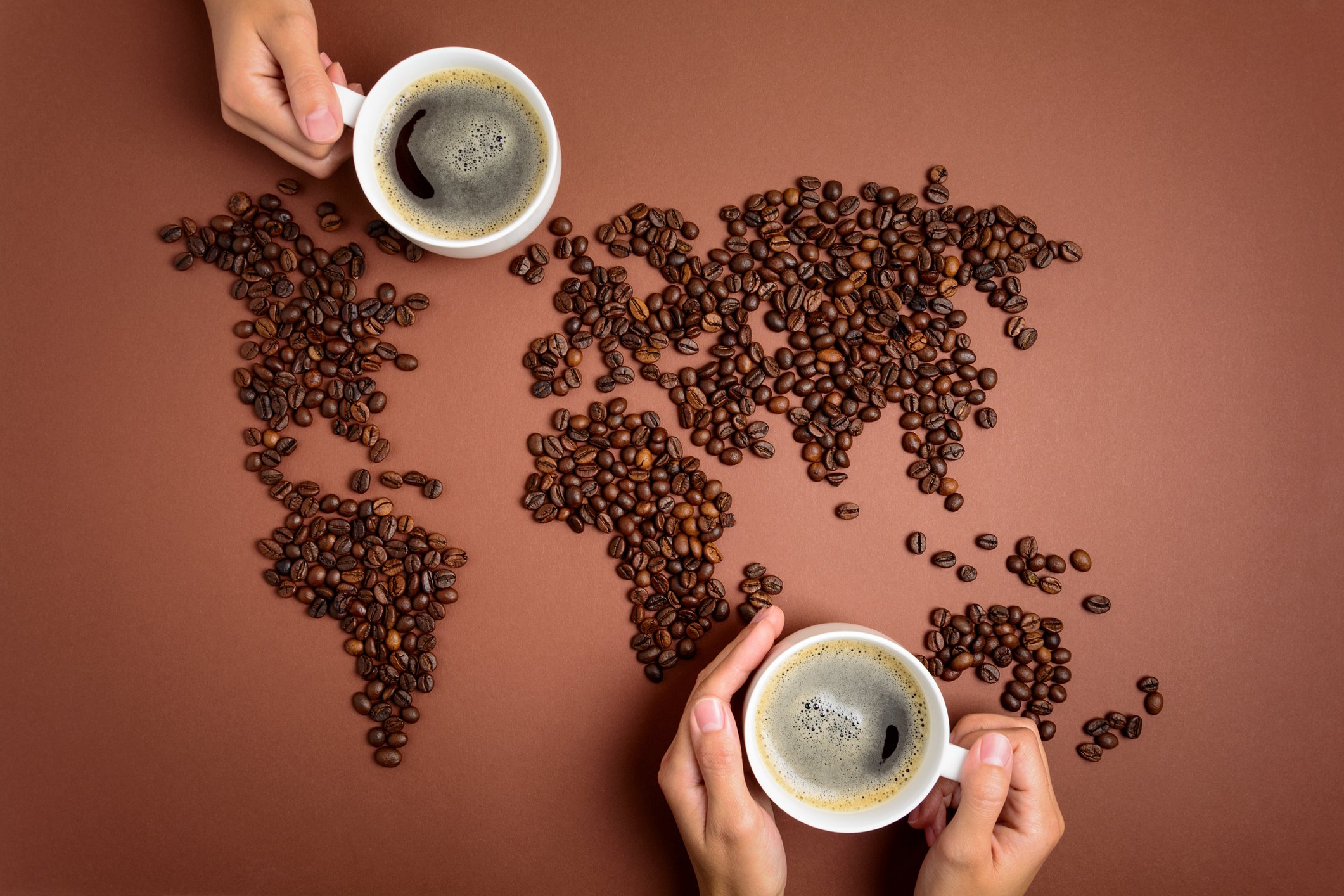 map of the world with coffee beans and two people drinking mugs of coffee