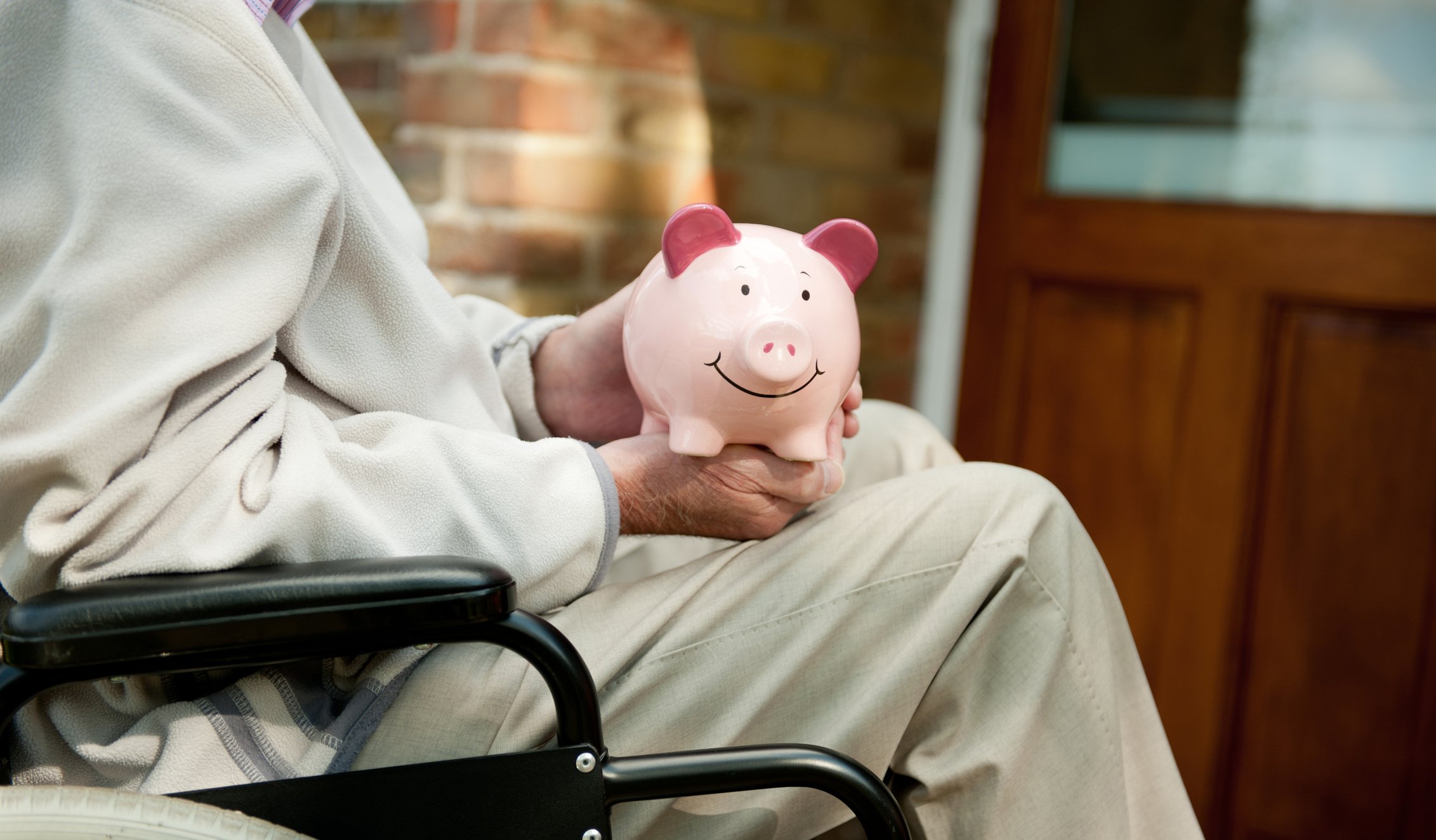A person in a wheelchair has a piggy bank on their lap.