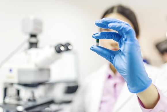A scientist holding a pill with a gloved hand.