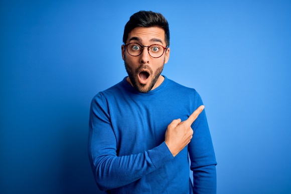 Person with shocked facial expression pointing index finger to the side.