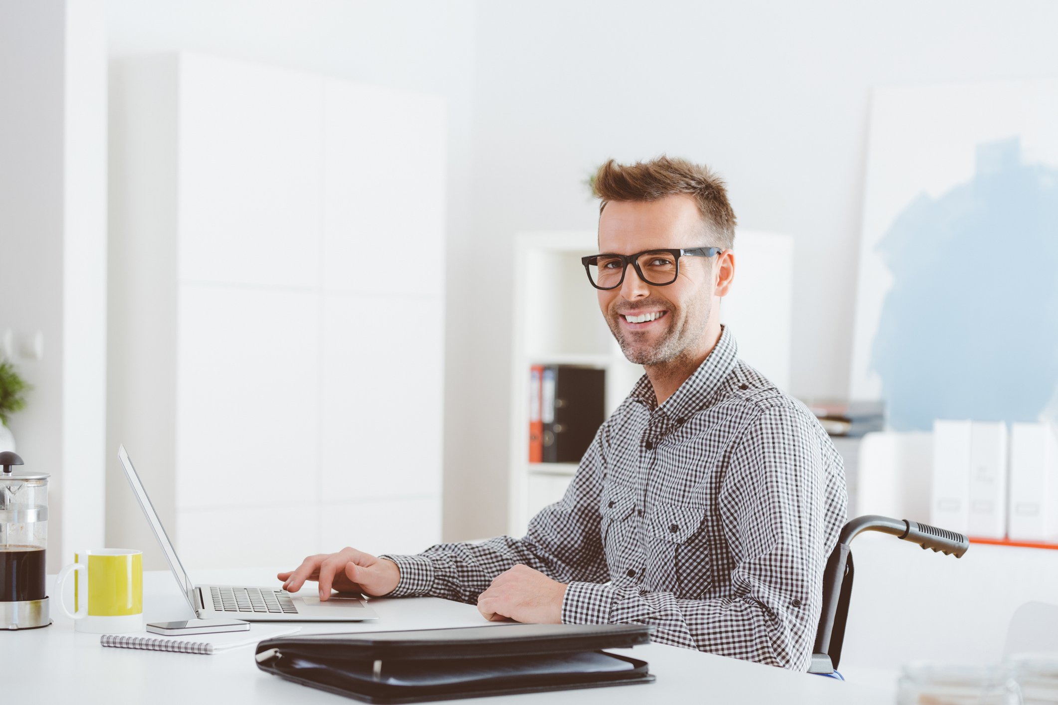 A person is at a desk with a laptop, smiling at the camera.