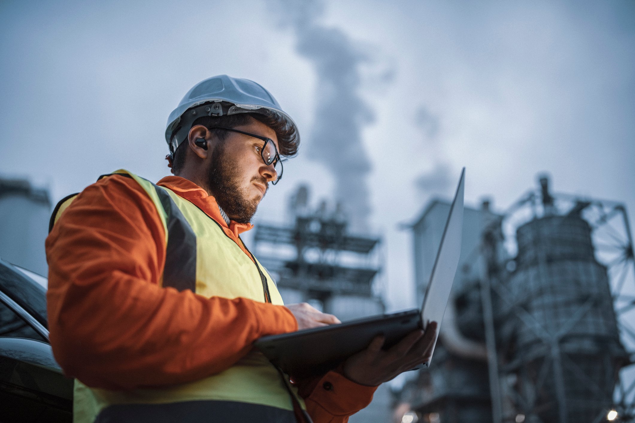 An engineer checks a laptop on the site of an industrial plant.