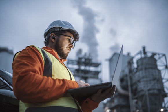 An engineer checks a laptop on the site of an industrial plant.