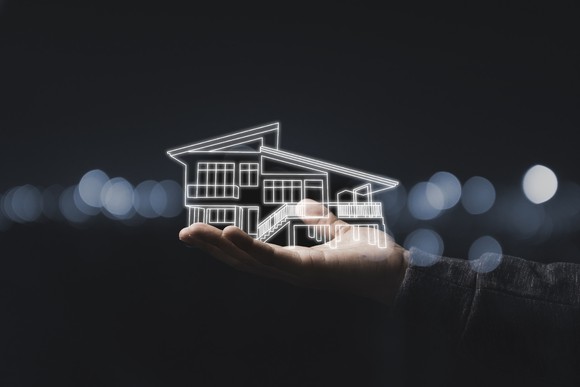 Hand holds a hologram rendering of a house. 