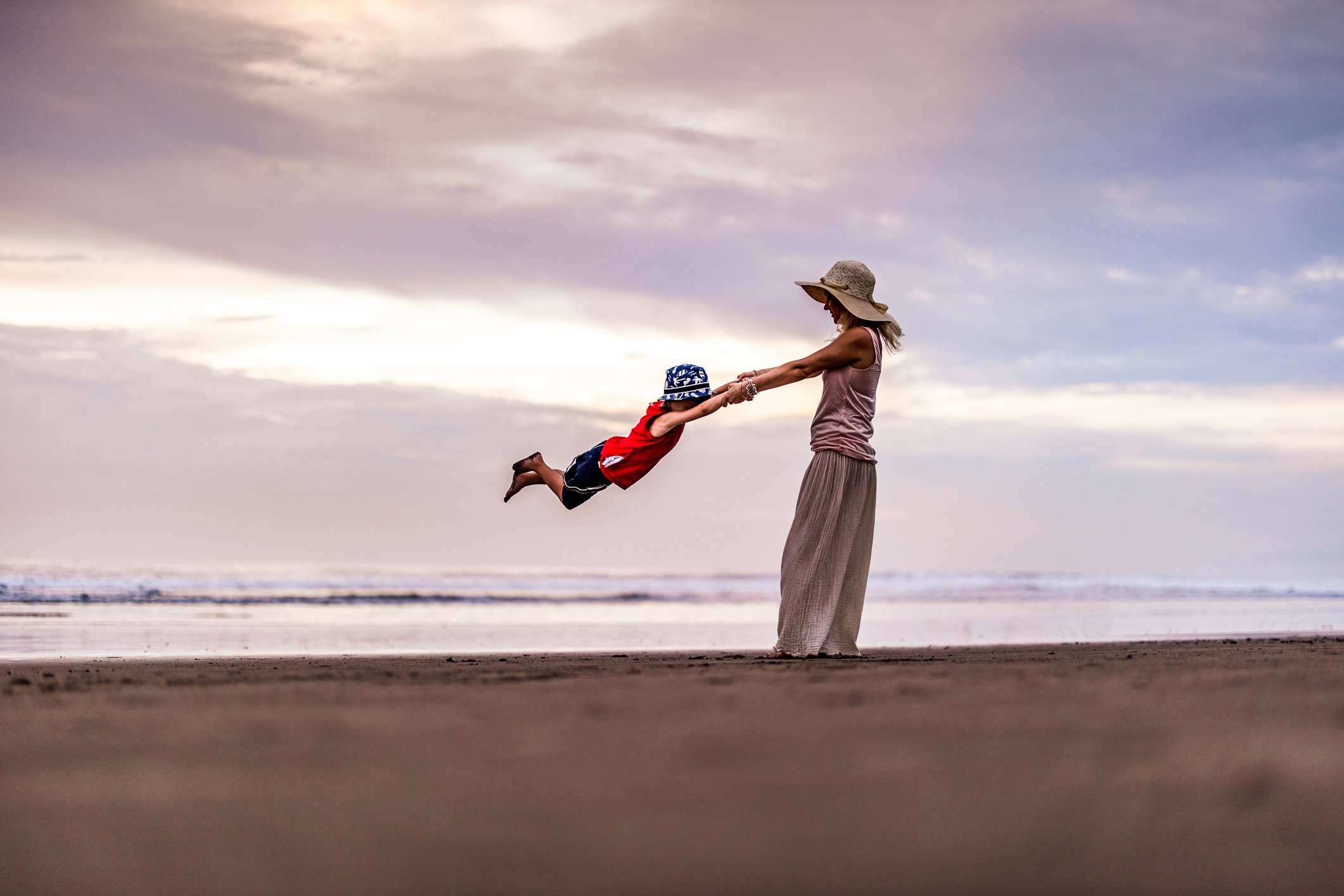 Person swings child around in an "airplane ride" on a beach at sunset.