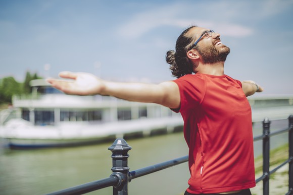 A smiling person is outdoors, with arms outstretched.