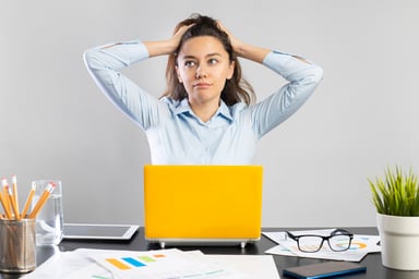A woman holds her head while sitting at a desk.