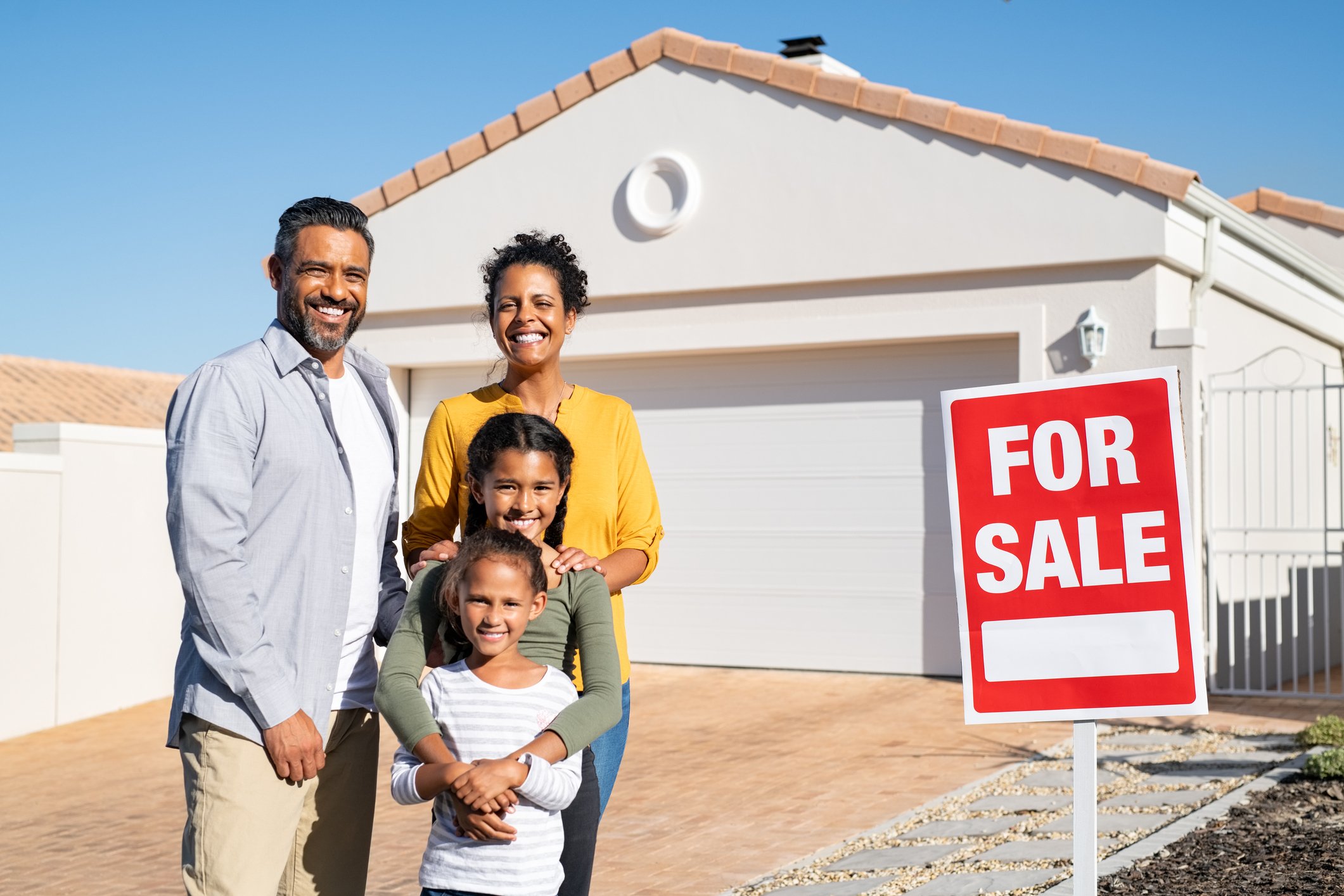 Family standing in front of a home with a for sale sign