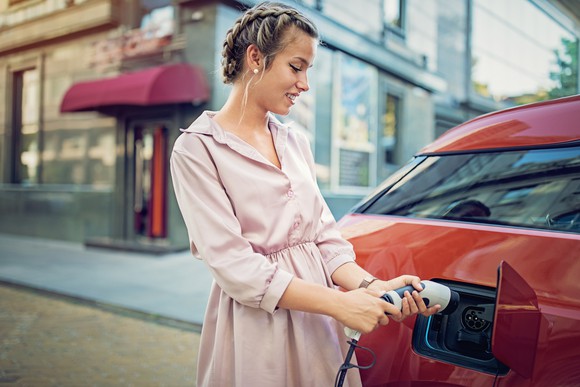 woman plugging charger into electric vehicle outside shopping area.