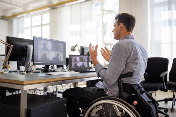 A man sitting in front of a computer with a videoconference displayed on the screen.