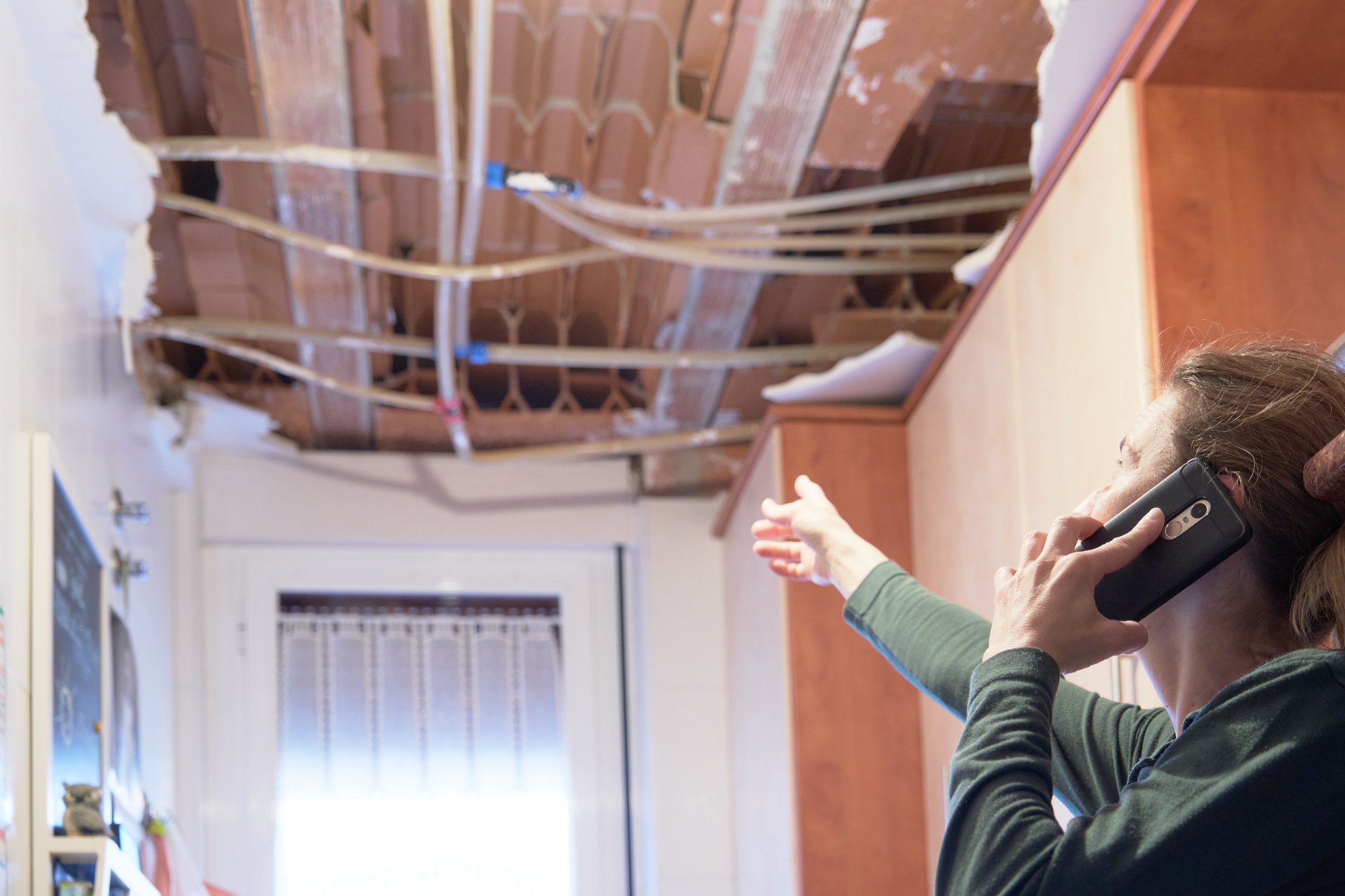 Person looking at damaged ceiling and talking on phone.