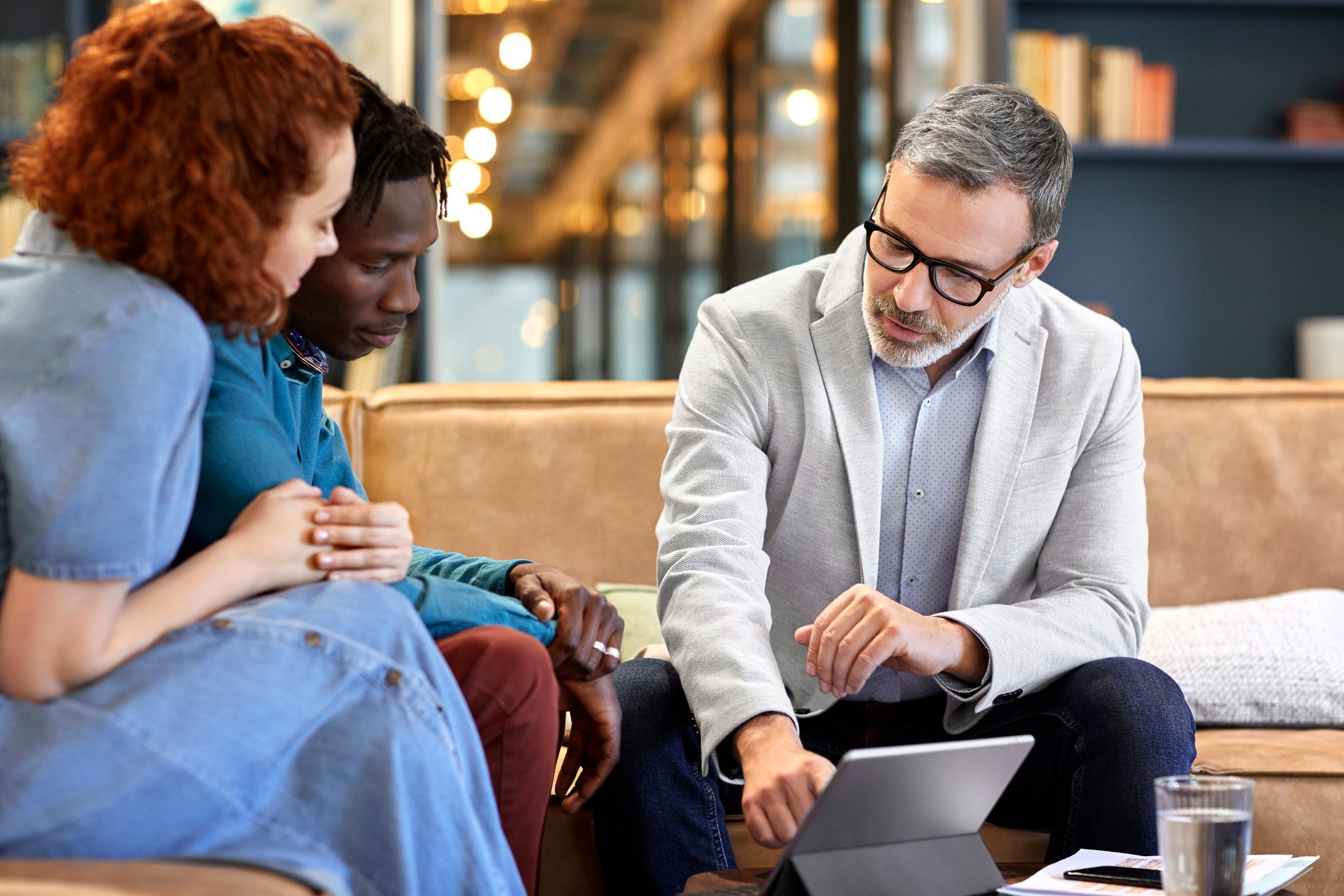 Three people sitting on couches nd looking at a tablet computer.