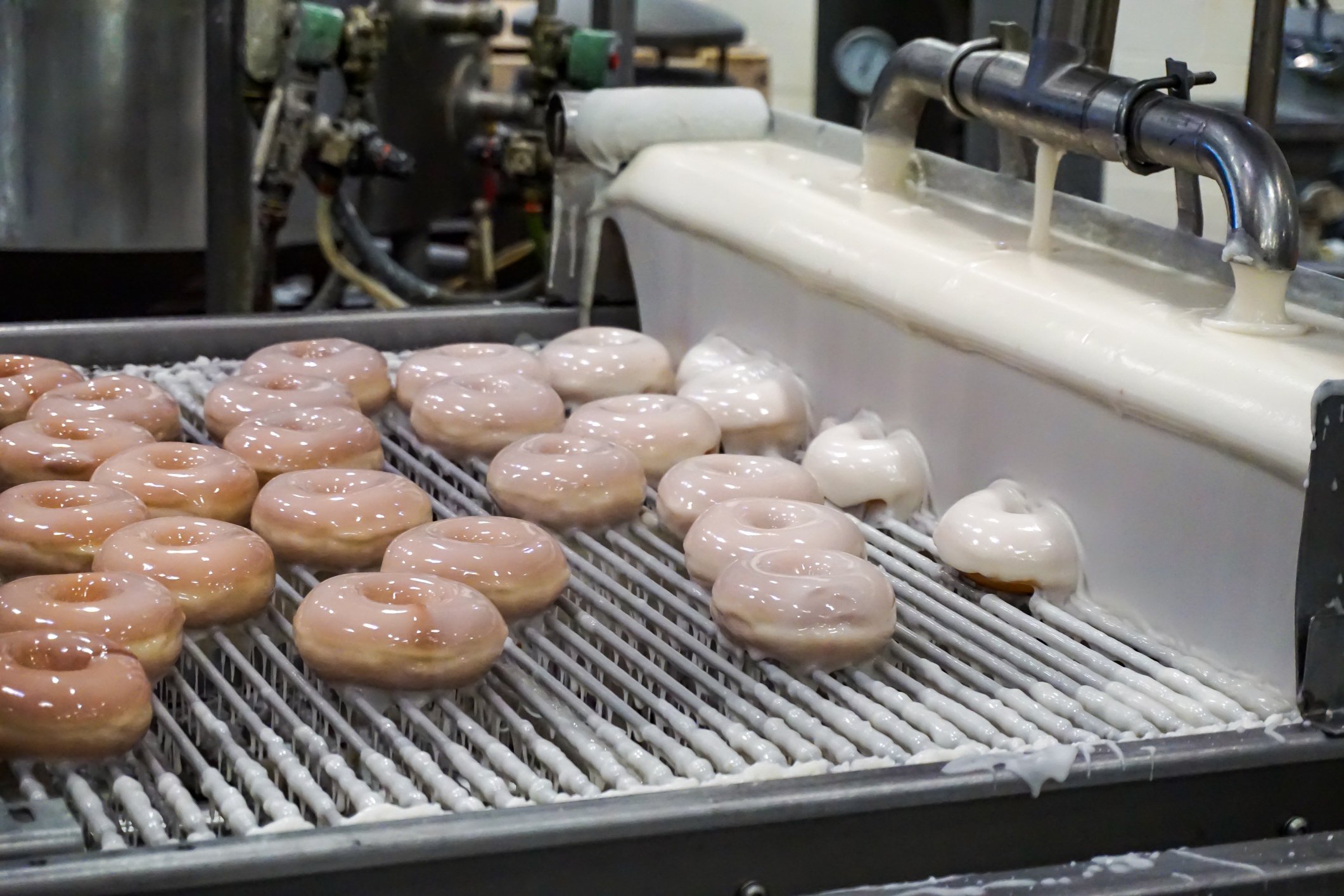 fresh baked donuts being covered in glaze. 