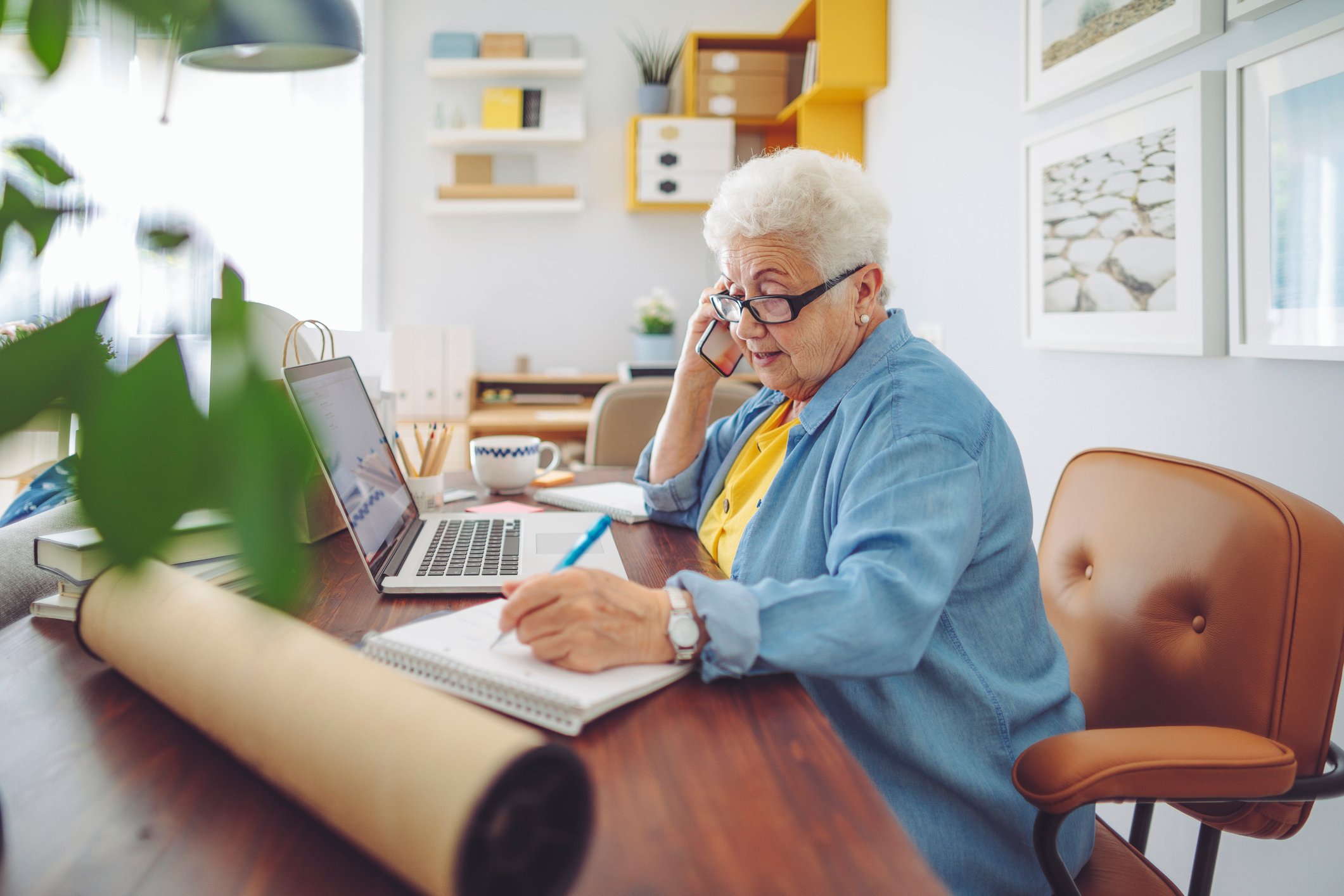 Person taking notes while on the phone in a home office setting.
