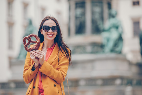 A cheerful-looking person in a yellow jacket holding a large pretzel.