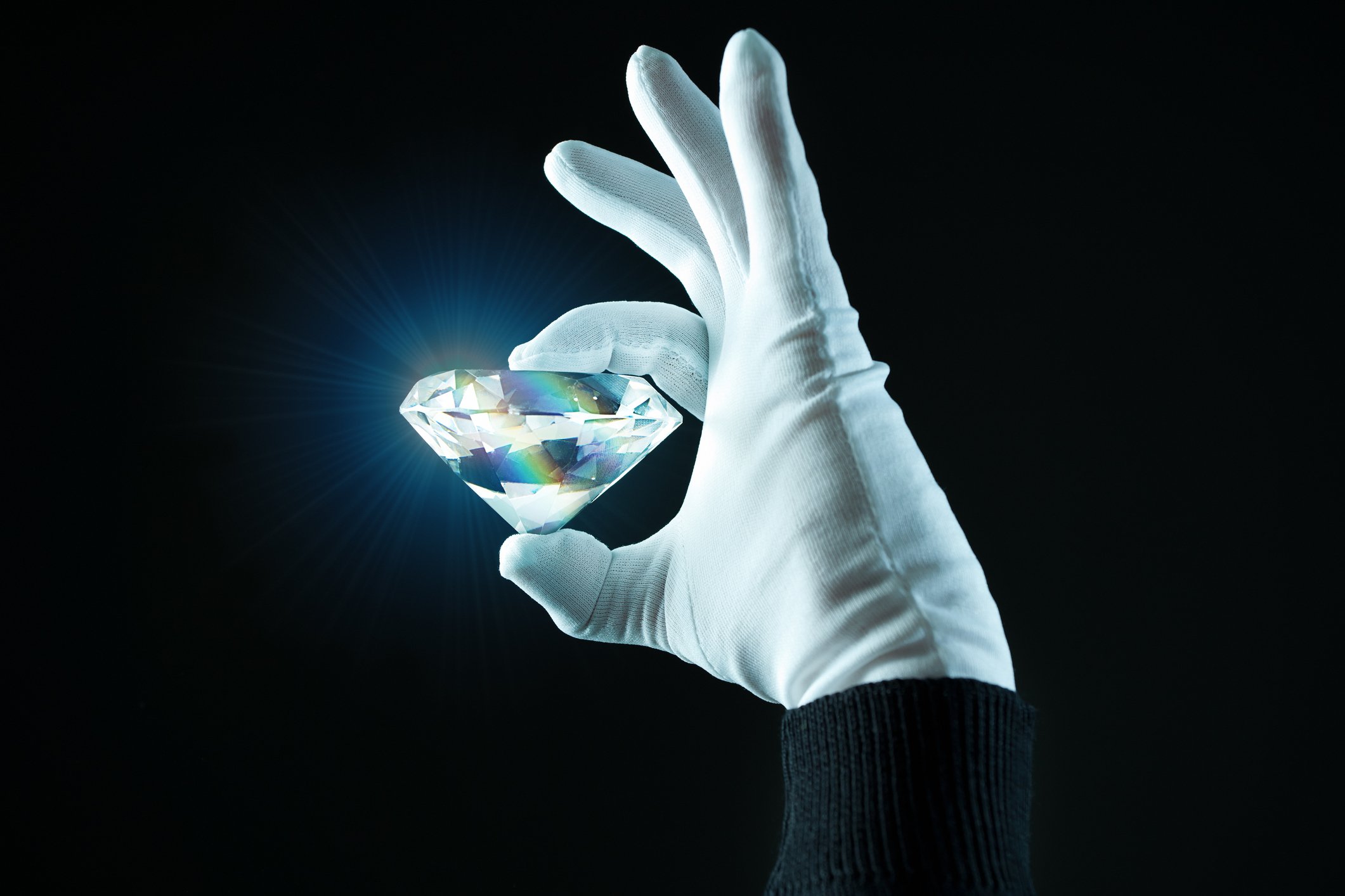 A hand in a white glove holding a huge, shining diamond against a black background.