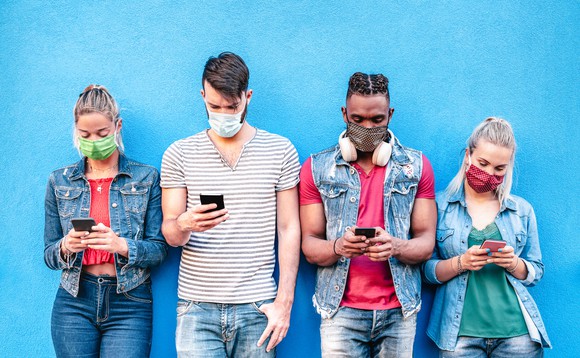 A group of young people wearing masks while checking their cellphones.