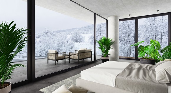 Luxury bedroom with glass walls and view of snow-covered trees.