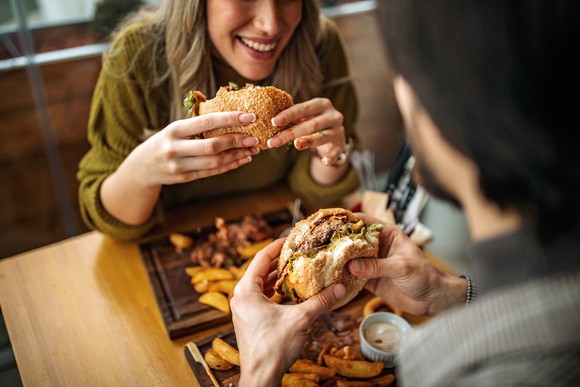 Two people eating burgers and fries in a restaurant.