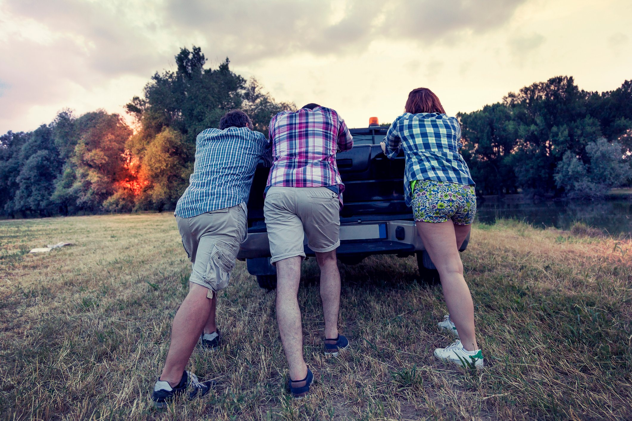 Three people pushing a pickup truck uphill.