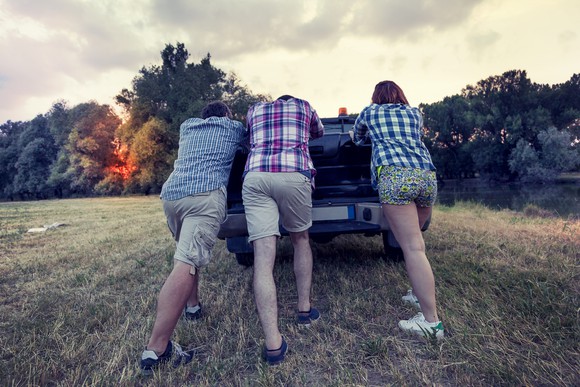 Three people pushing a pickup truck uphill.