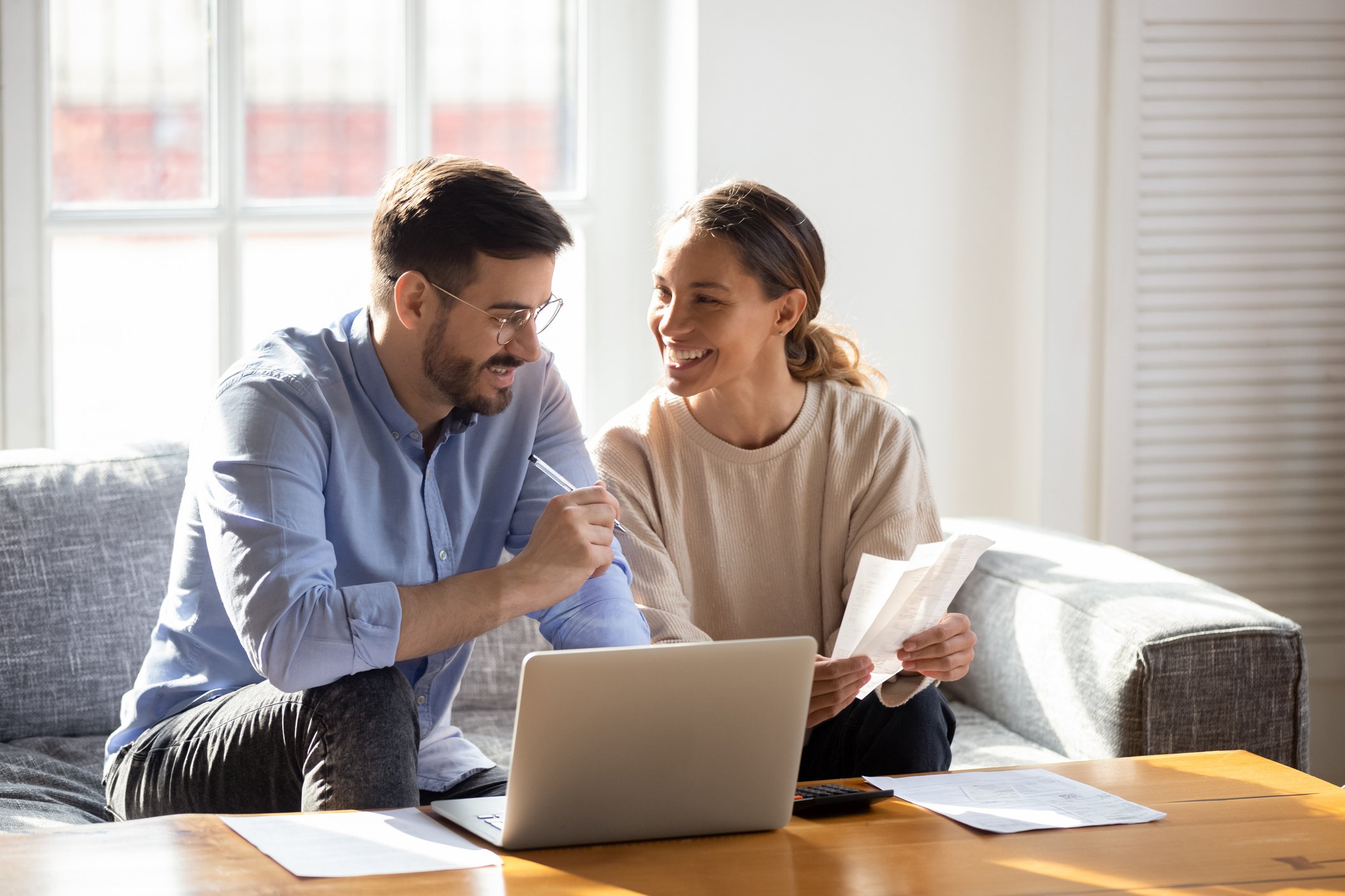 Adult couple smiling while looking over paperwork at home.