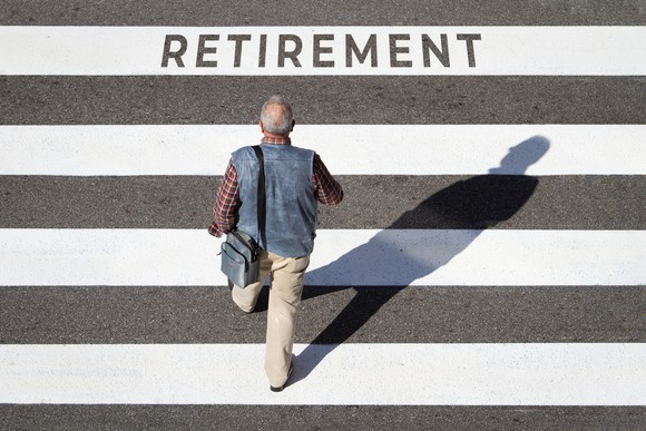 A person walking on a street with white lines painted on it and "retirement" spelled on one of the white lines.