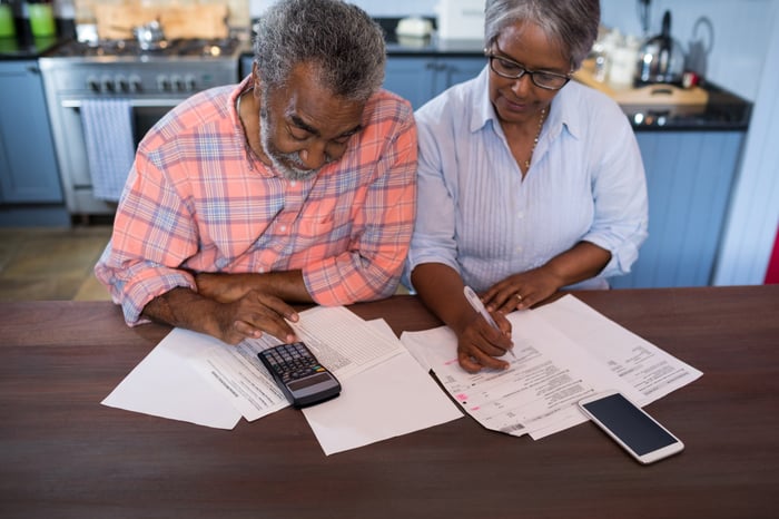 Two older people using calculator and reviewing papers.