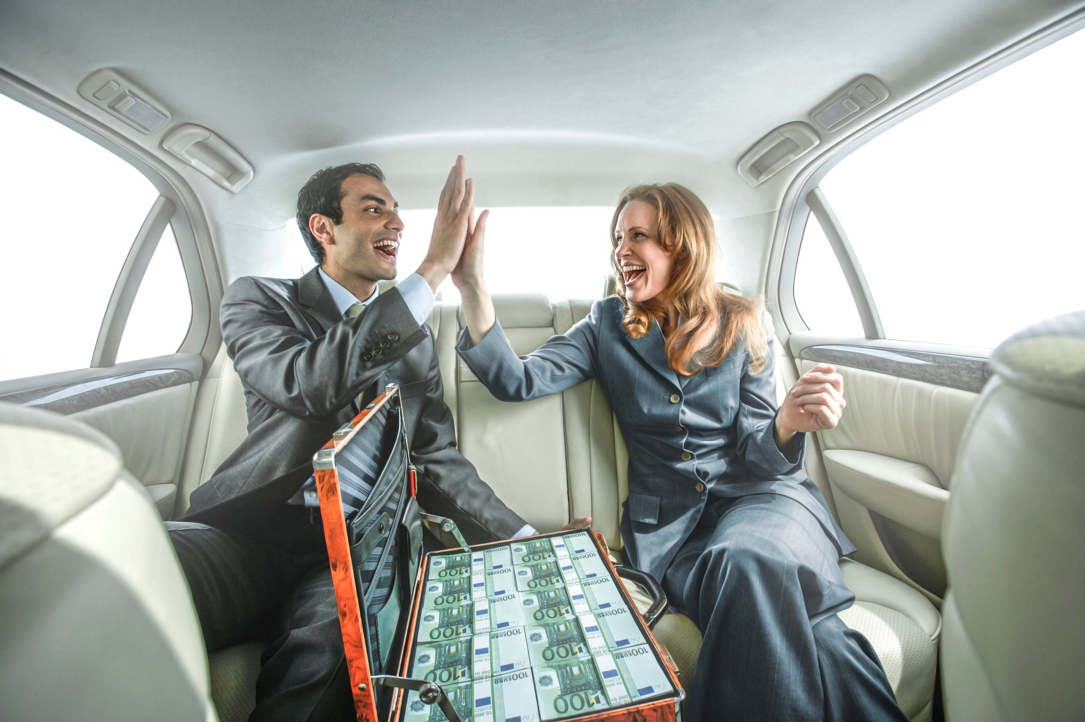 Two people high-fiving in a car with a bag of cash.