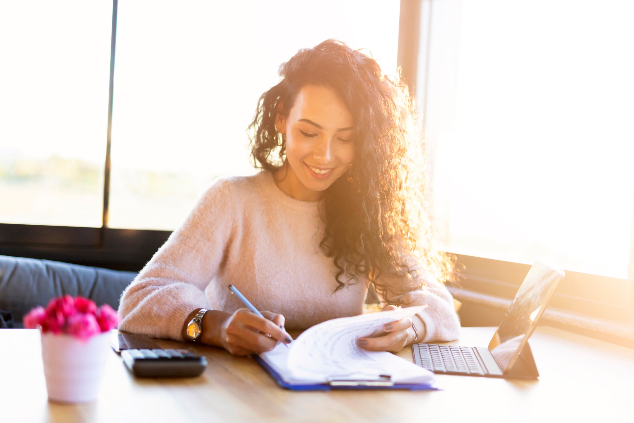 Woman reviewing paper-based financial documents, while also using a digital tablet.