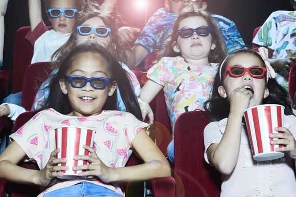 A group of kids eating popcorn and watching a movie in a movie theater.
