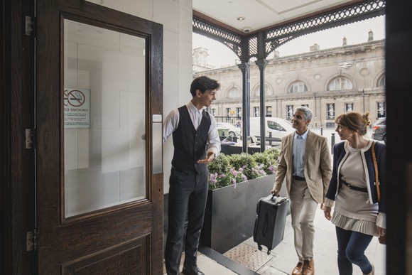 Two people greeted by a third at a hotel's entrance.