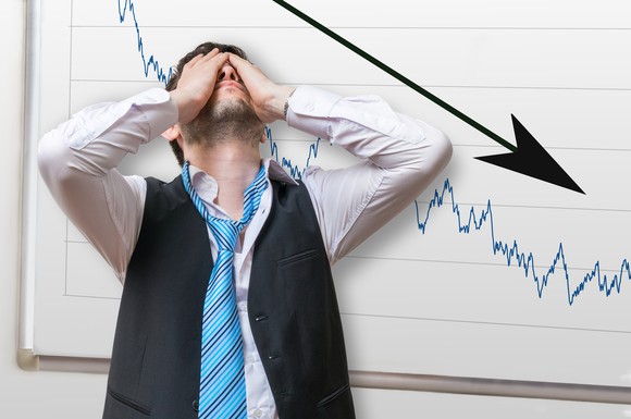 Person with hands over his eyes standing in front of a white board with a down arrow and stock chart heading down.