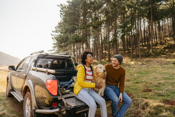 Two people and dog on truck tailgate.