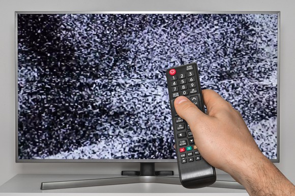 A hand points a TV remote at a modern big-screen TV, which shows a screen full of static.