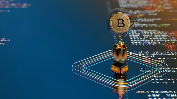 A digital illustration of a Bitcoin emerging from a screen.