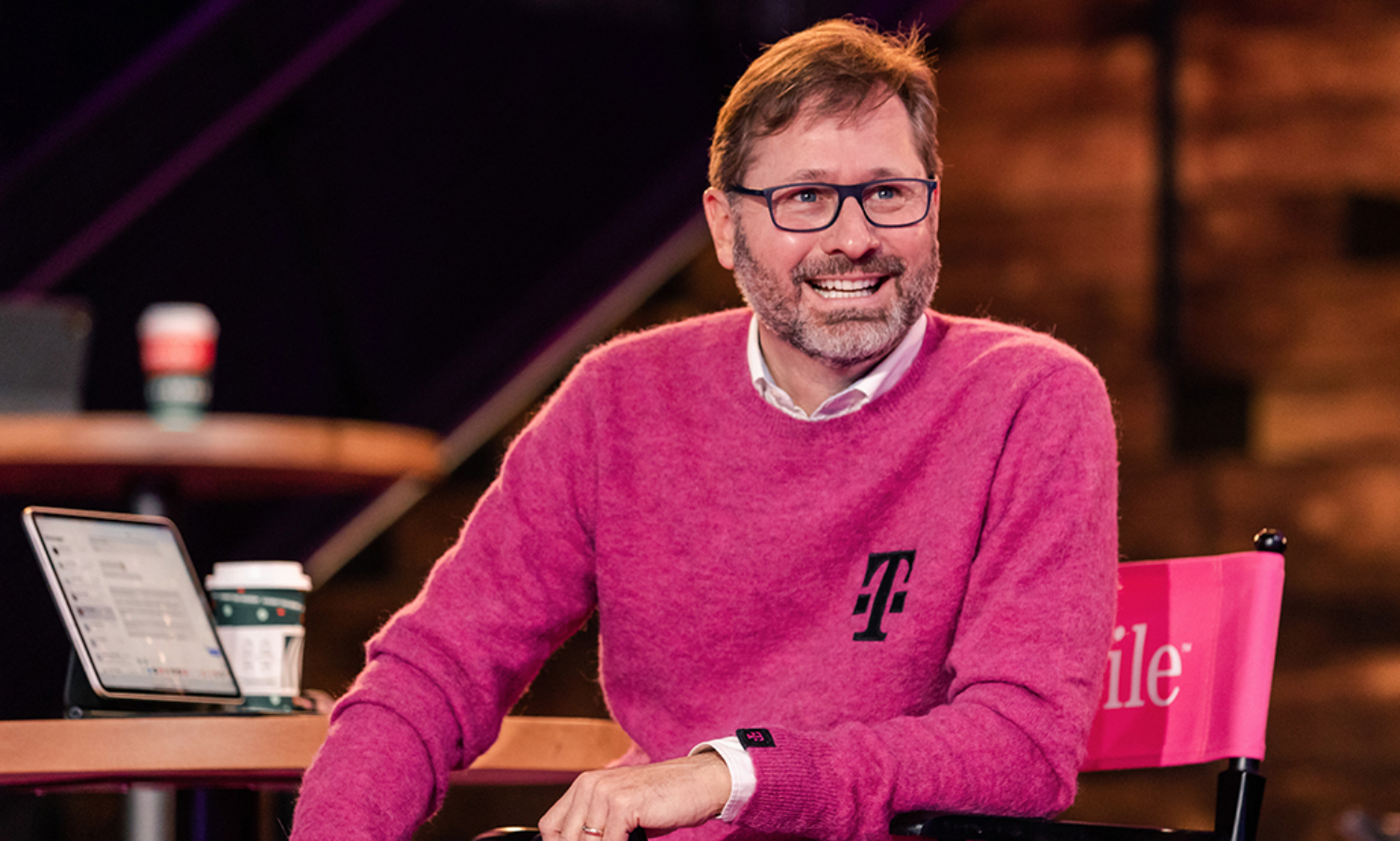 T-Mobile CEO Mike Sievert sits in a chair smiling. 