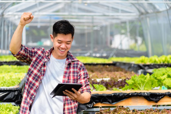 A hydroponics worker cheers news seen on a tablet.