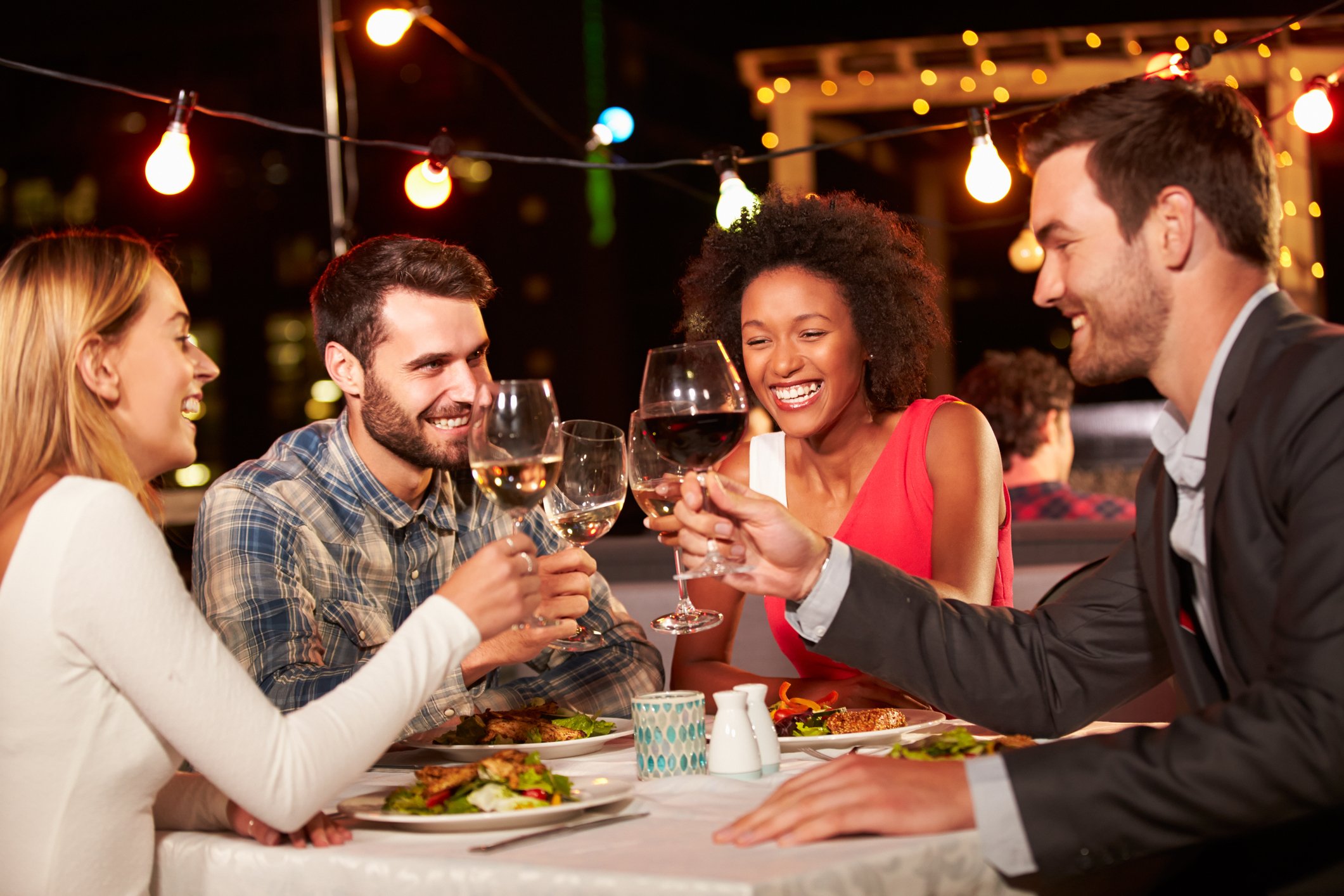 Four smiling people toasting and dining outdoors at night.