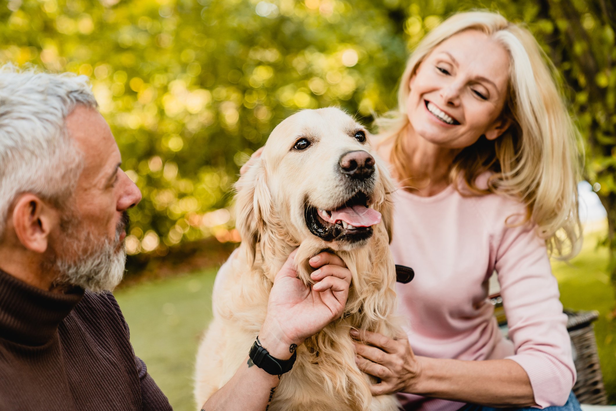 Middle-aged people sitting outside and smiling, with a dog.