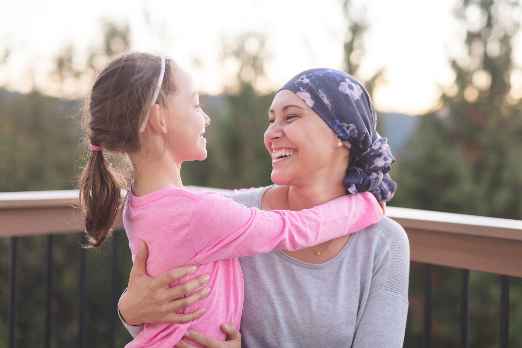 A cancer patient holds a child on a porch with trees in the background. 