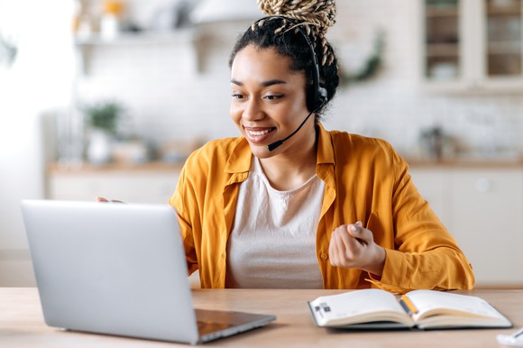 Smiling person wearing headset connected to a laptop computer.
